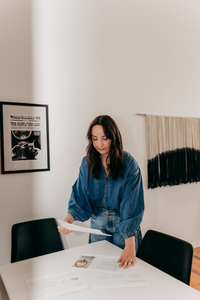 Delia McCowan, brand strategist, looking down at slides from her brand strategy deck, wearing a dark denim blouse, and medium wash jeans.